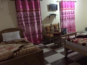 een slaapkamer met roze gordijnen en een bed en een tafel bij Hotel Pine Track in Dargai