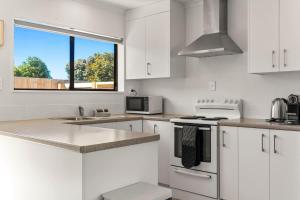a white kitchen with white cabinets and a window at Within Range in Papamoa