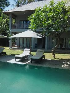 een huis met een zwembad met stoelen en een parasol bij Ju'Blu Hotel in Lovina