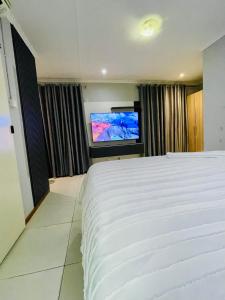 Que Self Catering Apartments - Block7 في غابورون: غرفة نوم بها سرير أبيض كبير وتلفزيون بشاشة مسطحة