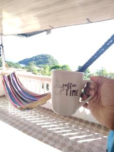 Casa Wili Taboga في تابوغا: شخص يحمل كوب قهوة أمام أرجوحة