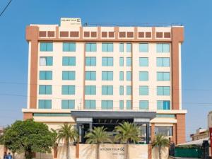 a large building with palm trees in front of it at Golden Tulip Kukas Jaipur in Jaipur