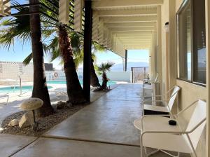 een veranda met stoelen en palmbomen en een zwembad bij The Gateway Boutique Vacation Rentals in Desert Hot Springs