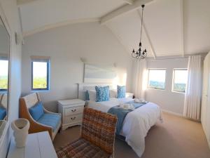a bedroom with a bed and a chair and windows at Romansbaai Beach House in Gansbaai