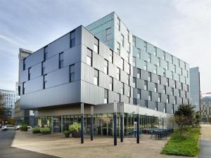 Un gran edificio de cristal con mesas en un estacionamiento. en Radisson Hôtel Bordeaux Saint-Jean, en Burdeos