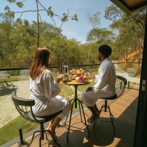a man and a woman sitting at a table with food at Chalé com banheira, piscina e cachoeira privativa in Taubaté