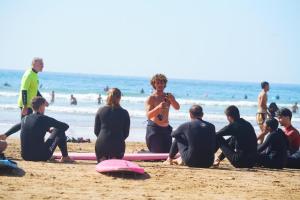 Tamazirt Surf Shop & School في تغازوت: مجموعة من الناس جالسين على الشاطئ