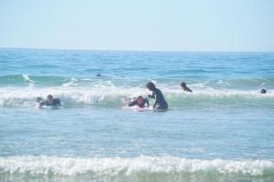 Tamazirt Surf Shop & School في تغازوت: مجموعة من الناس يسبحون في المحيط +صورتان