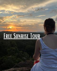 a woman sitting on a cliff watching the sunset at Sigiri Village Vibe Hostel in Sigiriya