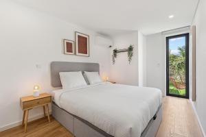 Una habitación blanca con una cama y una ventana en Private Garden Oasis, A Charming Flat in Bonfim, en Bicas