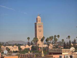 a tall clock tower with palm trees in front of a building at Riad Alaya, Rooftop Pool & Koutoubia View in Marrakesh