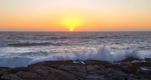 um pôr-do-sol sobre o oceano com ondas a bater nas rochas em Playas de Quintero em Quintero