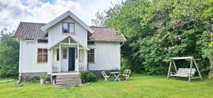 Charming house with kayaks, 300m from the sea on Orust SE09139 في Svineviken: منزل أبيض صغير به كرسيان وأرجوحة