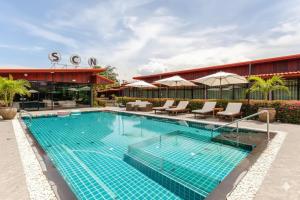 Una piscina con sillas y sombrillas al lado de un edificio. en Wellness Resort Rayong Managed by the SCN resort and spa limited, en Ban Huai Pla Kang