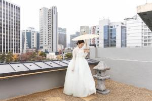 a woman in a white dress holding an umbrella on a roof at 율 한옥 호텔 in Samgong