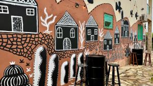 a wall with a painting of houses and stools at Hostel Ôxe in Paraty