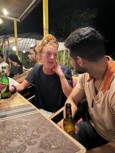 a man and a woman sitting at a table with a bottle of beer at The Peace Hostel in Arambol +46 photos