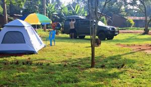 a blue and white tent and a truck and a tree at Risa Camping Site in Kiyunga