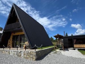 a house with a black roof and a stone wall at Cabana A-Frame Sesu in Cîrlibaba +8 photos