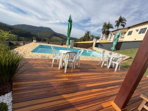 Una terraza de madera con mesas y sillas junto a una piscina. en Chalé Requinte da Serra, en Miguel Pereira
