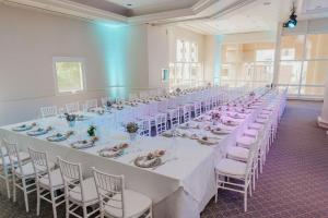 Un largo salón de banquetes con mesas y sillas blancas. en Lucania Palazzo Hotel, en Comodoro Rivadavia