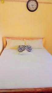 ein weißes Bett mit einer Uhr an der Wand in der Unterkunft Swahili BNB Homes in Kilifi