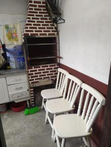 three white chairs in a kitchen with a brick wall at Casa Temporada Caraguatatuba in Caraguatatuba