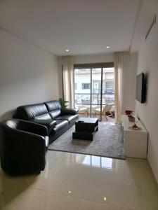 a living room with a black leather couch and a television at super studio in Aïn Harrouda