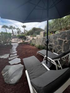 a patio with two lounge chairs and an umbrella at Oasis de paz junto al mar in Maspalomas