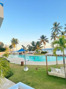 a swimming pool with palm trees and a beach at Las Olas Apartment, Juan Dolio in Guayacanes
