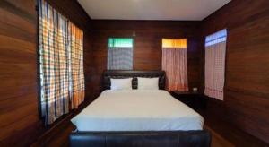 a bedroom with a bed with wooden walls and windows at The Frog Khao Yai Resort in Ban Tha Chang