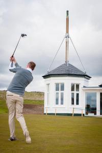 a man swinging a golf club in front of a house at Ingleside Cottage in Elie