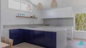 een keuken met blauwe kasten en een wastafel bij Oceanview Beach House in Caves Beach