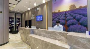 Lavande Hotel Wuhan Hanjiang Road Liuduqiao Metro Station في ووهان: رجل يقف خلف منضدة في غرفة بها زهور أرجوانية