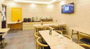 GreenTree Inn Shanghai Railway Station Macao Road في شانغهاي: غرفة بها طاولات وكراسي وتلفزيون على الحائط