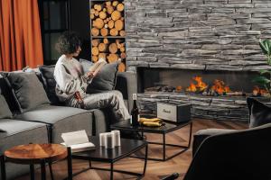 a woman reading a book in a living room with a fireplace at Dialog Kokhta in Bakuriani