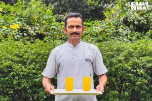 ein Mann hält ein Tablett mit einem Glas Orangensaft in der Unterkunft StayVista at The Vara House with AC & Board Games in Varanasi