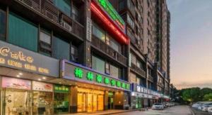 GreenTree Inn Jiaxing ZhongHuan South Road Zhonggang City Express Hotel في جياشينغ: مجموعة مباني عليها لافتات نيون