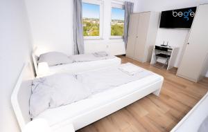 a white bedroom with two beds and a window at BEGE APARTMENTS LightHaus in Holzwickede