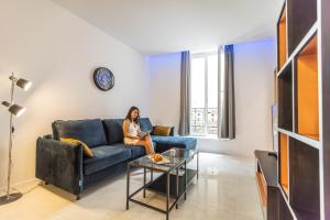 a woman sitting on a blue couch in a living room at Residence Meynadier - apartments - New - AC - Wifi - Close Beach and Palais - LRA Cannes in Cannes