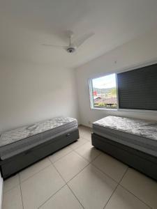 two beds in a room with a window at Apartamento pé na areia no centro de Bertioga in Bertioga