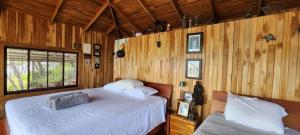 two beds in a room with wooden walls at Teak house in a forest above the beach 