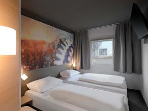 two white beds in a room with a window at B&B HOTEL Willich in Willich