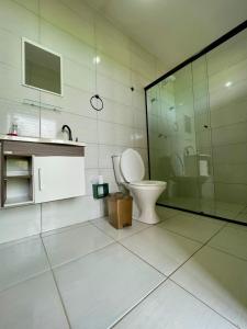 a bathroom with a toilet and a glass shower at Jardins do Rosa - Hospedagem e Entretenimento in Imbituba
