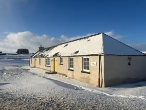 een oud gebouw met een gele deur in de sneeuw bij Calsie Cottage, Clatt in Kirktown of Clatt