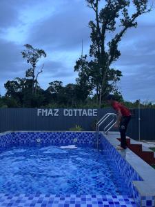 a man is standing next to a swimming pool at FMAZ Cottage in Kampong Gong