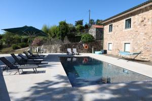 a swimming pool with chairs and an umbrella next to a building at Qt Refúgio de Rubiães Villa 1-2 Paredes de Coura in Paredes de Coura