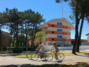 two people riding bikes down a street with a building at Residence Silver Sail in Bibione