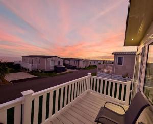 Sea View Chalet Steps from Durdle Door Sleeps 6 في ويست لولوورث: شرفة منزل مع غروب الشمس في الخلفية