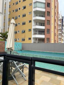 a umbrella and a chair next to a swimming pool at Apt completo: ar cond piscina e academia no Centro in Taubaté
